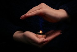 Close-up of female hands holding a burning candle in the dark. Selective focus.