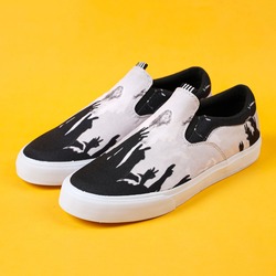 Pair of black shaded white sneakers with white edges all over, facing the sides. The color combination of white slip-ons against a yellow background creates a gorgeous color contrast. 