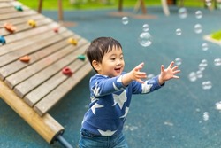 Little Asian boy is playing on the playground with happy face in summer and happily running around with soap bubbles