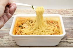 Instant noodles with dry vegetables and spices with red pepper in disposable container with plastic fork. Traditional cheap Asian food. Fast food, most popular. Selective focus, blurred background