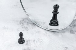 Black chess pawn in front of mirror sees reflection of chess queen. The concept of career growth, transformation. Proverb illustration: soldier who doesn't want to be general is bad soldier