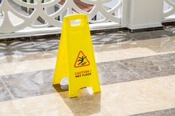 Yellow warning sign Caution Wet Floor on a marble floor in a public area. Preventing injuries to hotel guests during wet cleaning of halls and public places.