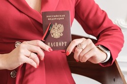 Passport of a citizen of the Russian Federation in the hands of a woman. The hands of a woman in a red dress hold a Russian passport and a pen.