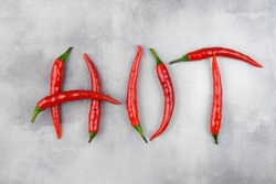 The inscription HOT is laid out from pods of red hot chili peppers on an abstract gray background. Creative image of spices.