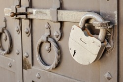 Large metal padlock on a heavy metal door with a deadbolt. Antique padlocked door