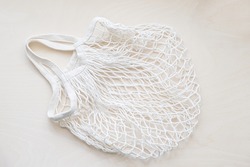 Eco friendly mesh bag on a light wooden background. String bag made of white cotton threads. Zero waste lifestyle.