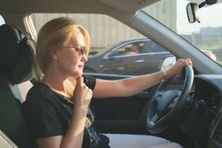 Young attractive woman drives a car. Profile photo of a beautiful blonde woman with long hair wearing sunglasses. Woman in a car while driving.