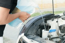 Woman pours windshield cleaning fluid. Flow windshield fluid into the windshield washer reservoir. Water tank wiper on car engine room, Maintenance concept.