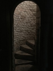 Medieval stone spiral staircase, steps going up to ground floor. Medieval dungeon. Stone steps framed by arched doorway. Going down the basement of a castle. 