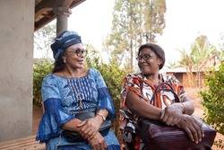 Two senior African ladies friends are sitting and chatting, African women traditionally dressed together, adult friendship concept