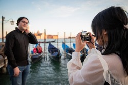 Girlfriend takes a photo of her boyfriend while they are on vacation in Venice, tourists visiting the city of love