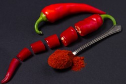 Red ground pepper next to a whole red hot pepper on a black background. Chili pepper isolated