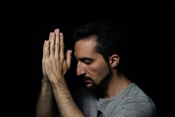 The man folding his hands in prayer to god on a black background. prayer to God for happiness and a better life. Repent of your sins. Unity with God	