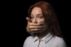 A man's hand covers the girl's mouth on a black background. The concept of domestic violence and sexism.