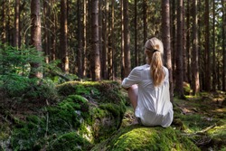 Woman sitting in green forest enjoys the silence and beauty of nature.