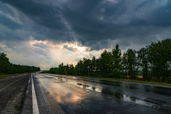 wet asphalt road panorama in countryside on rainy summer day. autumn rain road puddle in forest under dramatic cloudy sky