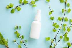 White cosmetic spray bottle and birch branches with young small leaves on blue background. Mockup branding. Skincare beauty and liquid antibacterial spray. Natural Body mist. Front view, flat lay.