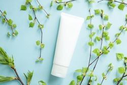 Top view of mockup of white squeeze bottle plastic tube for branding of medicine or cosmetics - cream, gel, skin care. Cosmetic bottle container and birch branches with small leaves on blue background