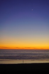 Lonely man in sunset on the coast of Pacific Ocean. Moon in the sky