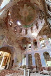 View of the middle part of the old ruined and abandoned Orthodox church in Russia. The dome is fully visible. Closed windows. Peeling paint and old red bricks. Daylight.
