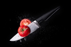 Fresh ripe tomato cutting with a knife and flying in motion on the black background with red splashes