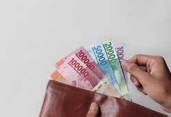 a man's hand takes and shows money from a wallet isolated on white background, rupiah is the currency of Indonesia
