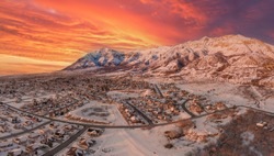 Aerial drone view high above the neighborhoods of North Ogden and Pleasant View Utah with an incredible orange winter sunset and fresh fallen snow, no people, panorama 