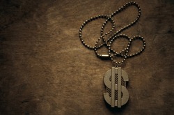 A gold chain with a dollar sign on a wooden table in vintage style. Gangster jewelry on a chain. The dollar symbol in gold.