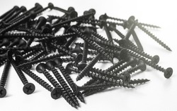 Black metal self-tapping screws on wood on a white table. Long black screws on drywall.