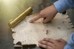 The child's hand points to the place of the buried pirate treasure on the map. A quest for children in the fresh air. A game of pirates. Children's holiday.