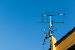 Old analog television aerial transmission antenna on the roof of house in clear blue sky. Obsolete tv and radio communication and broadcasting technology.