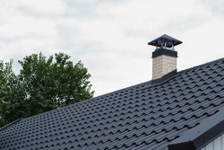 Roof with metal tile dark and chimney, metal roofing shingles. The roof of the metal dark color with a chimney on a background of cloudy sky.