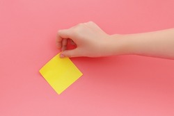 Woman's hand glues yellow sticker or sticky post-it notes on pink background.