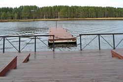 The pier and marina on pontoons reflecting in the water, with a walkway between the handrails against the backdrop of a pine forest.
