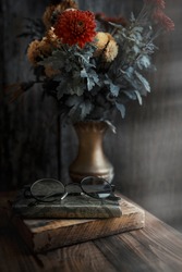 autumn bouquet of flowers is on the table next to glasses and a book