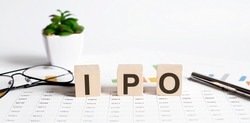 IPO word concept written on wooden blocks, cubes on a light table with flower ,pen and glasses on chart background