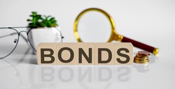 BONDS concept on wooden cubes and flower ,glasses ,coins and magnifier on twhite background