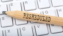 Text RESHEDULED on wooden pencil on white keyboard. Business