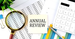 ANNUAL REVIEW text on sticker on diagram with magnifier and calculator. Business