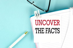 UNCOVER THE FACTS text on sticky on notebook with pen and glasses , blue background