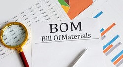 BOM - Bill Of Materials text with magnifying glass lens on office desk table.