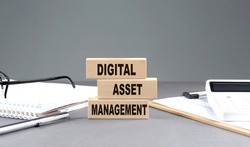 DIGITAL ASSET MANAGEMENT text on a wooden block with notebook,chart and calculator, grey background