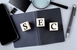 Word SEC on wooden block on a black notebook with smartpone, credit card and magnifier