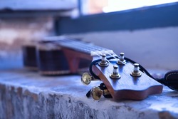 Detail of the pegbox, fret and strings of a brown ukulele with strap leaning against a brick window frame. Concept instruments, music, strings.