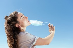 Breathing and feeling free during Coronavirus pandemic concept. Young woman removing a protective surgical mask.