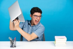 Angry hispanic student throwing laptop isolated on blue background