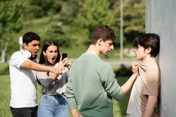 Teenager bully menacing boy while friends are recording. Bullying and violence at school concept