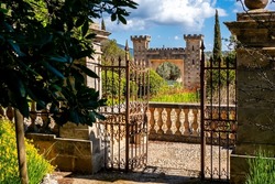 A rusty iron fence in front of a stonemade railing leads into a garden with verdant plants that surrounds the impressive entrance portal of the public manor called Raixa.