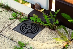 Balcony steel drain hole mesh and green leaves. Black metal Drainage grate for draining, directing excess water down into the sewers and prevent flooding. Dandelions sprouted between the tiles