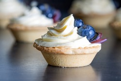 Berry tartlets with butter cream on a dark wooden background. Summer fruit baking. Tartlets with blueberries